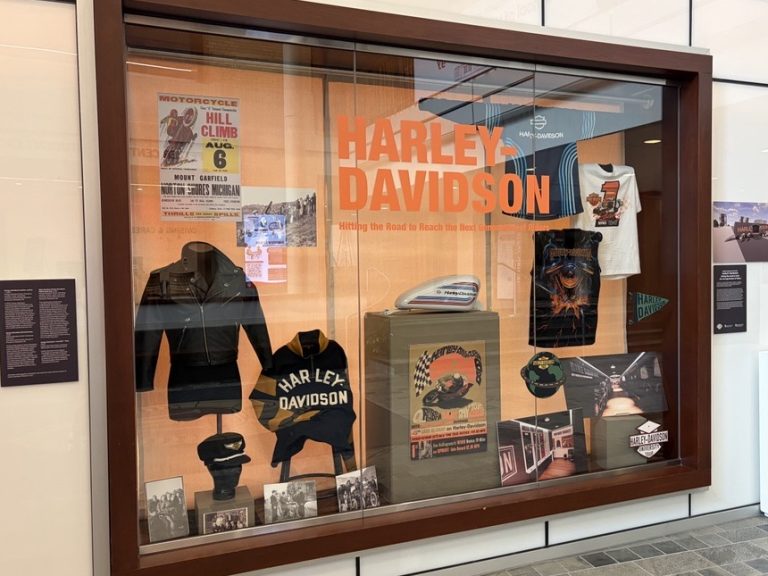 Window display of Harley Davidson merchandise, with graphics created by undergraduate Human Ecology students. Harley Davidson text on the window in bright orange.